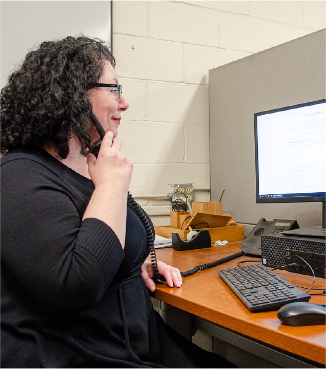 A woman at an office desk taking a pick-up request by phone.